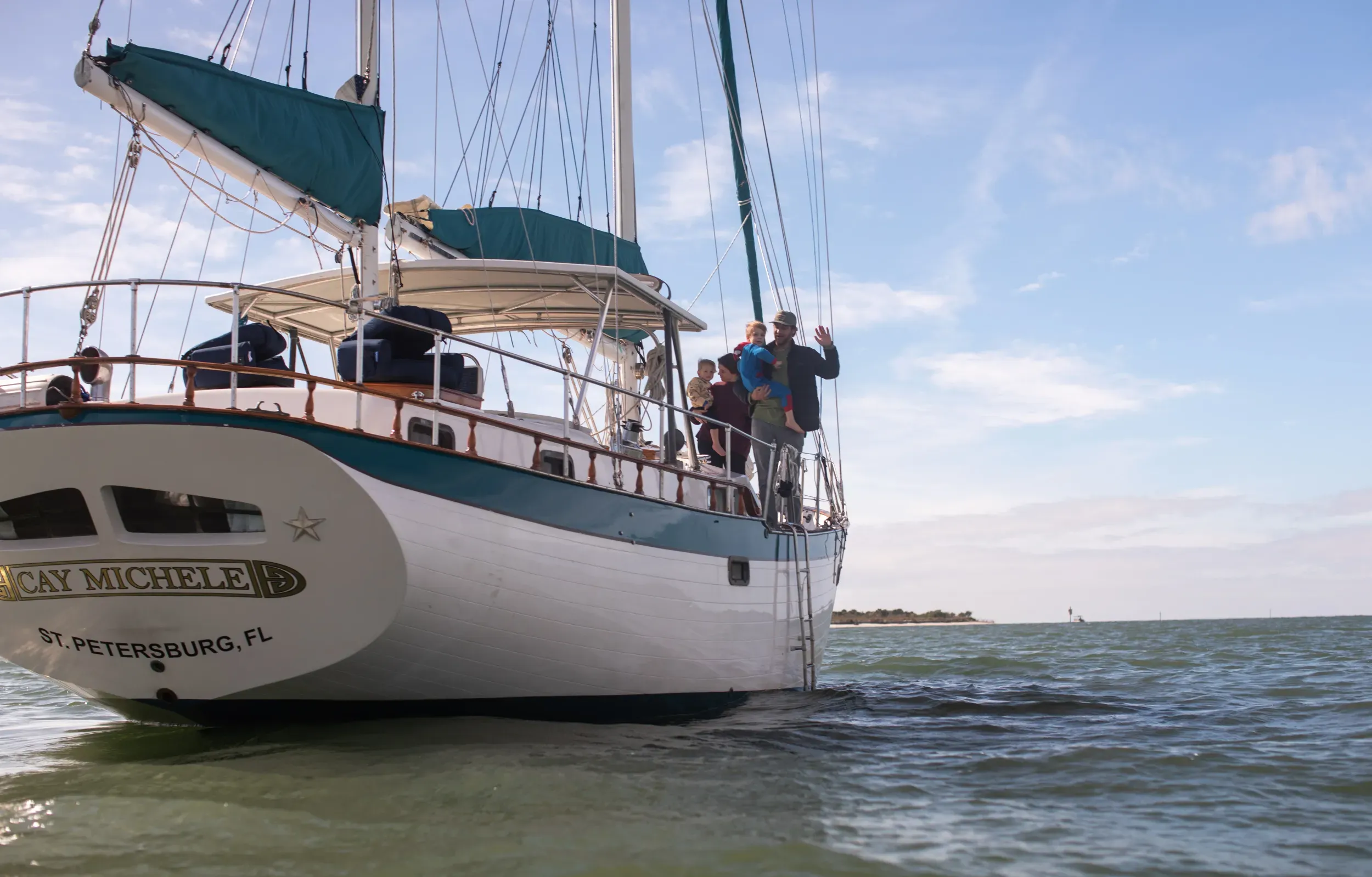SV Cay Michele at anchor near a barrier island with guests waving from the stern